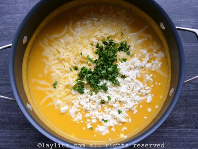 Uma panela cheia de sopa cremosa de couve-flor, guarnecida com queijo e coentro picado.