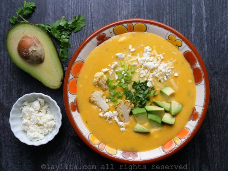 Sopa cremosa de couve-flor com batatas e queijo servida em uma tigela florida sobre uma mesa de madeira escura.