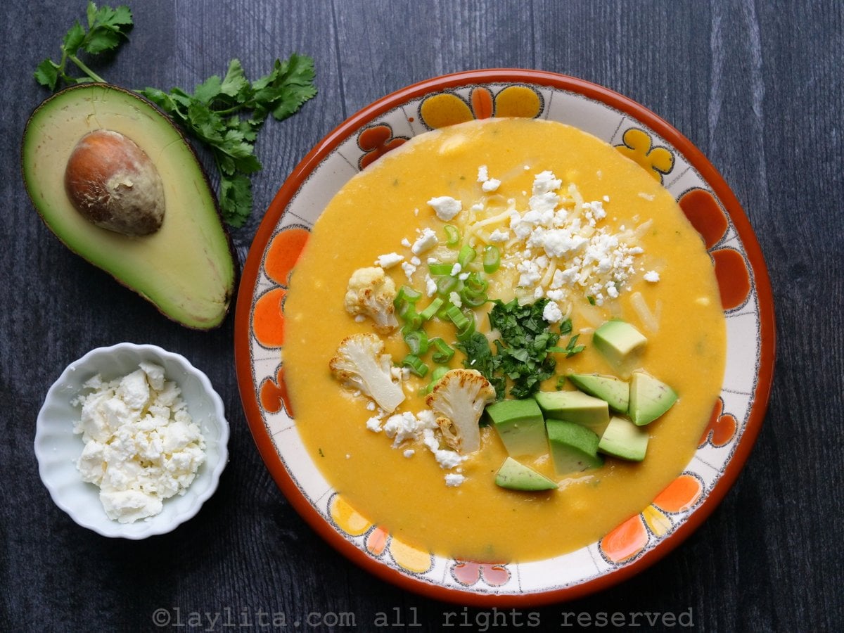 Sopa cremosa de couve-flor com batatas e queijo servida em uma tigela florida sobre uma mesa de madeira escura.