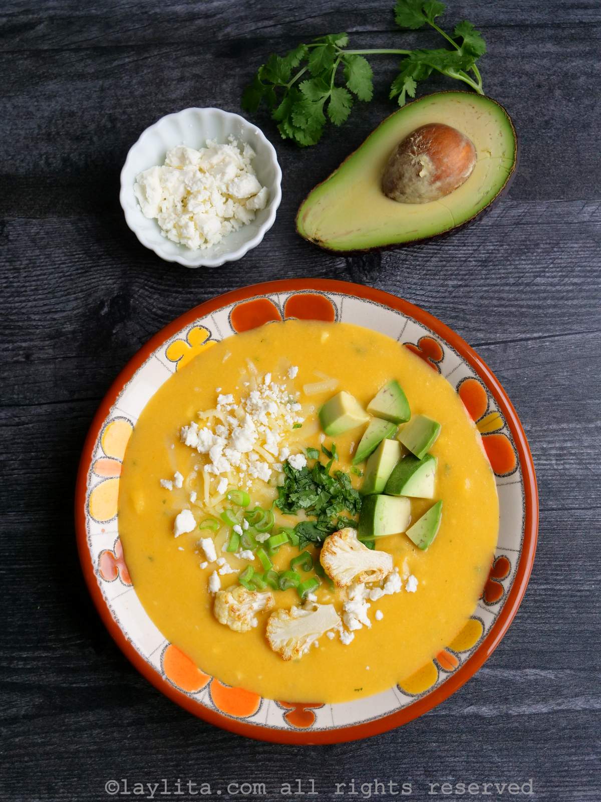 Uma tigela de sopa cremosa de couve-flor com batatas e queijo, guarnecida com queijo, coentro e abacate.