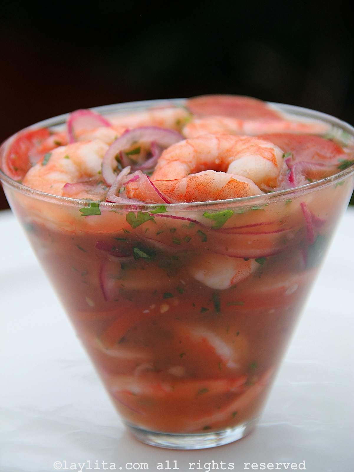 Una copa llena de ceviche de camarones con cebolla y tomate