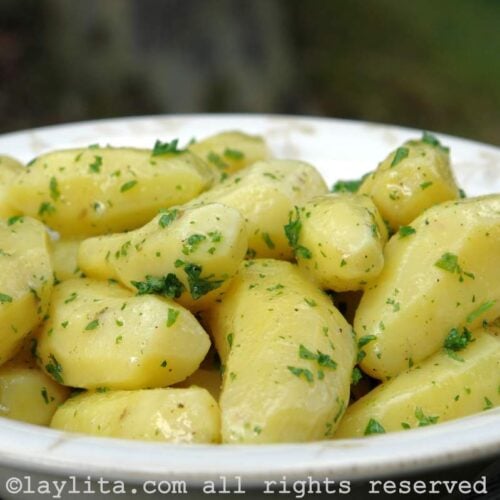 Un plato lleno de papas peladas y cocidas cubiertas con salsa de mantequilla y perejil