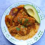 Seco de pollo con arroz amarillo, aguacate y plátanos fritos