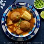 Un plato sopero con flores azules relleno de caldo de bolas de verde, al lado hay una servilleta, una rodaja de limón y cebollín picado