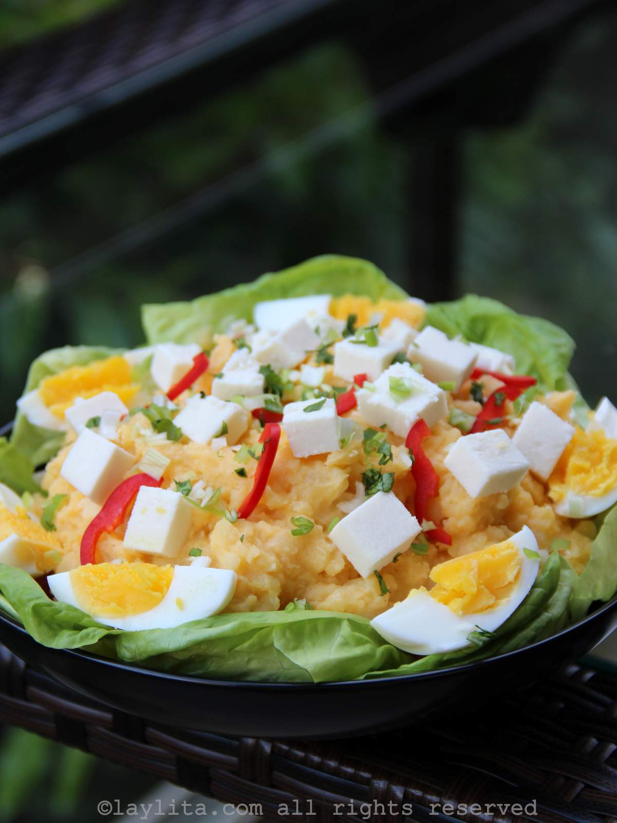 Un plato negro con hojas de lechuga y lleno de molo de papas decorado con huevos duros, queso fresco y tiritas de ají