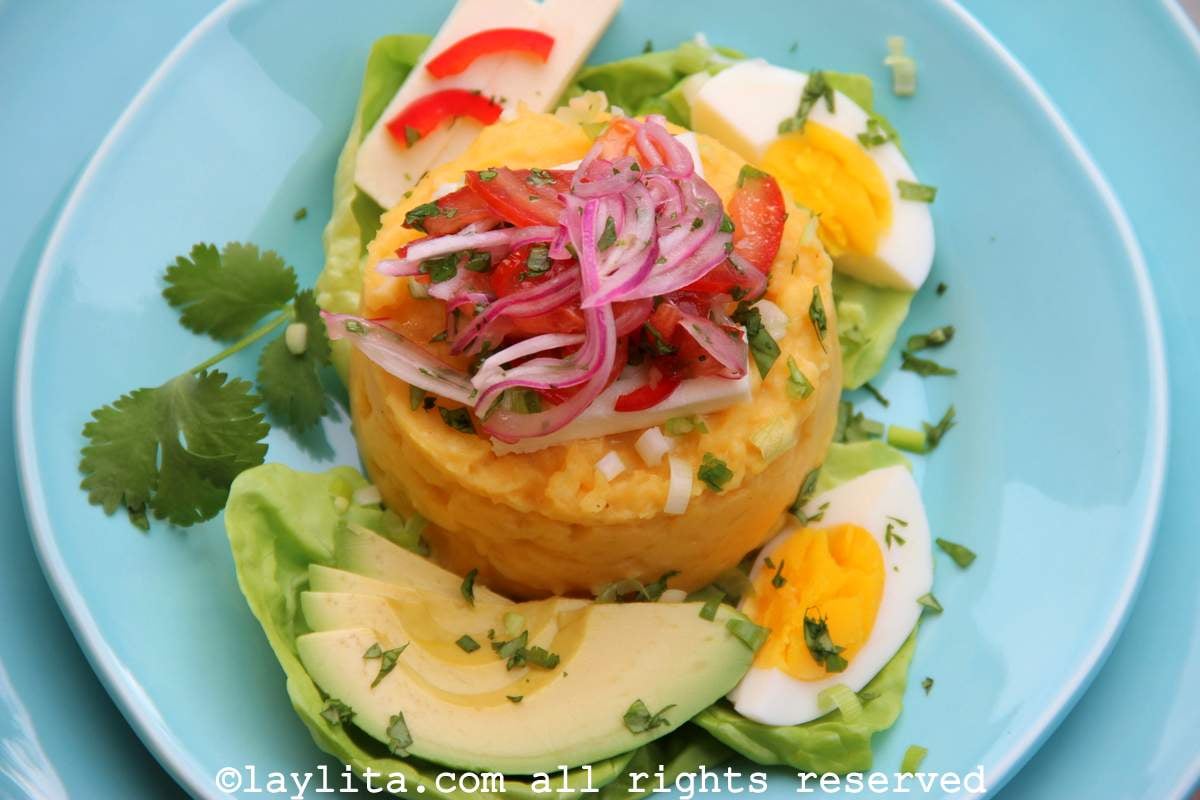 Un plato celeste con pure de papa decorado con curtido de cebolla, aguacate y huevo duro