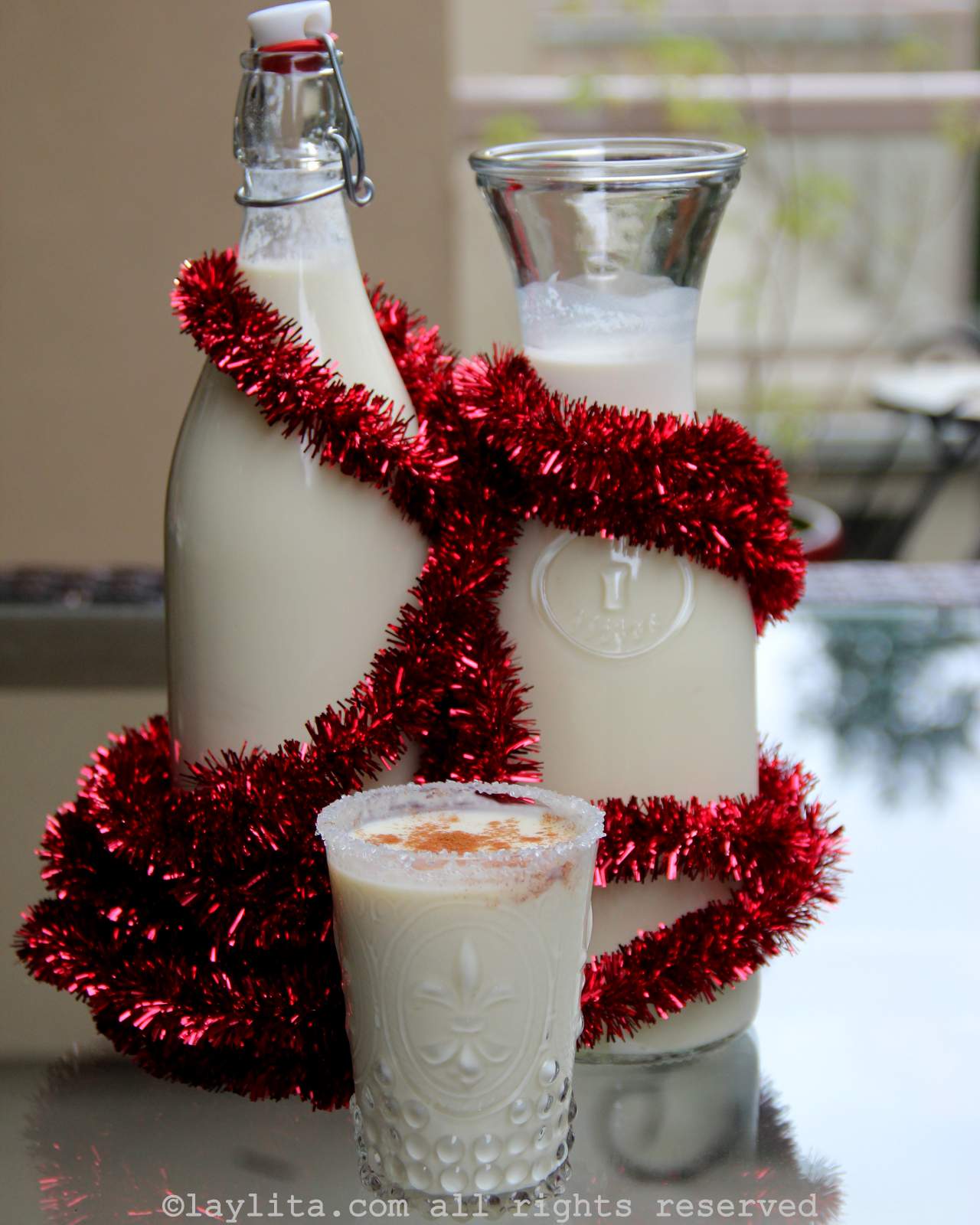 Dos botellas de rompope con una cinta roja y un vaso de rompope en el centro