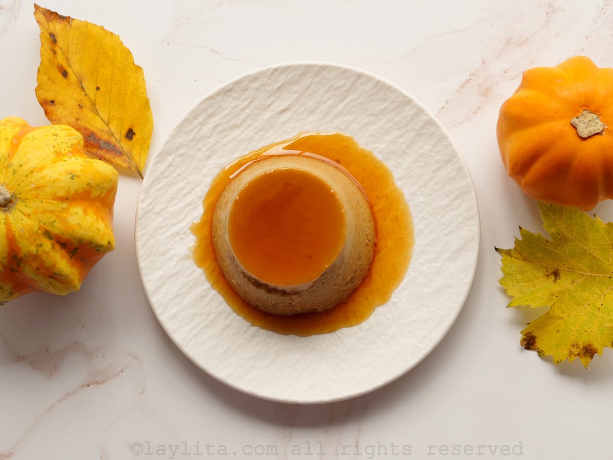 Un flan individual de calabaza en un plato blanco con calabazas y hojas decorativas a los lados