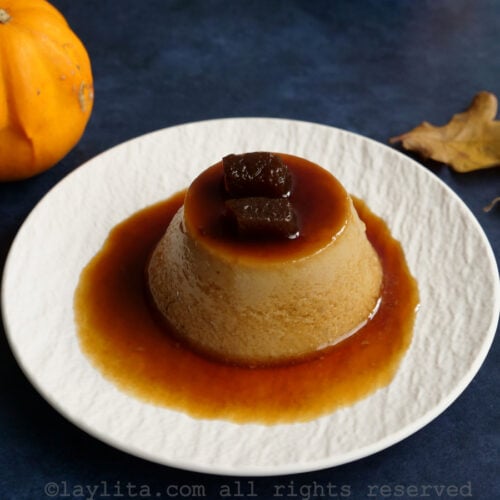 Un flan pequeño individual desmoldado en un plato blanco con calabaza confitada encima