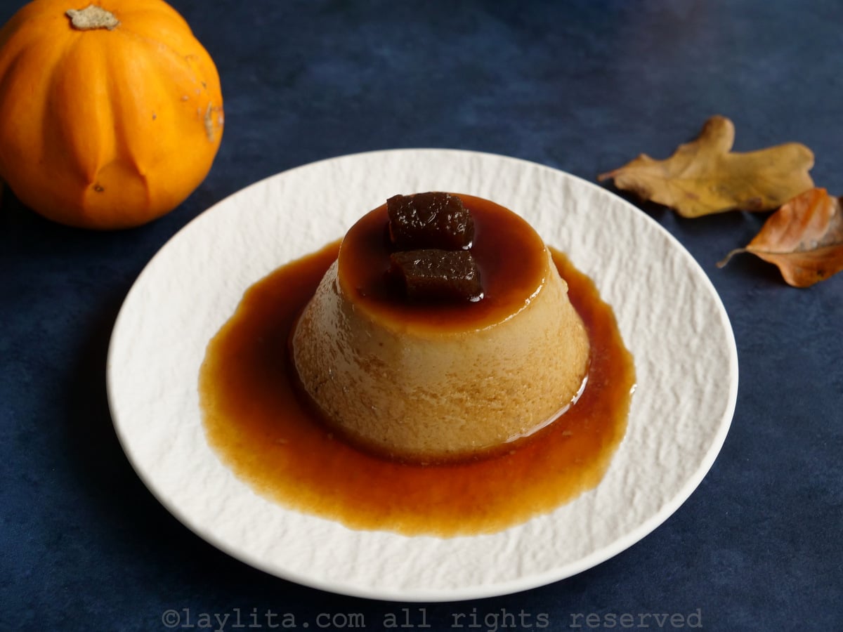 Un flan pequeño individual desmoldado en un plato blanco con calabaza confitada encima