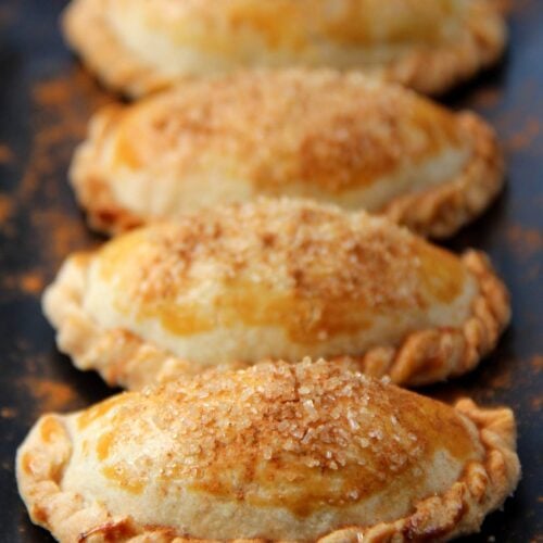 Cuatro empanadas dulces con relleno de calabaza y decoradas con canela molida en un plato rectangular negro