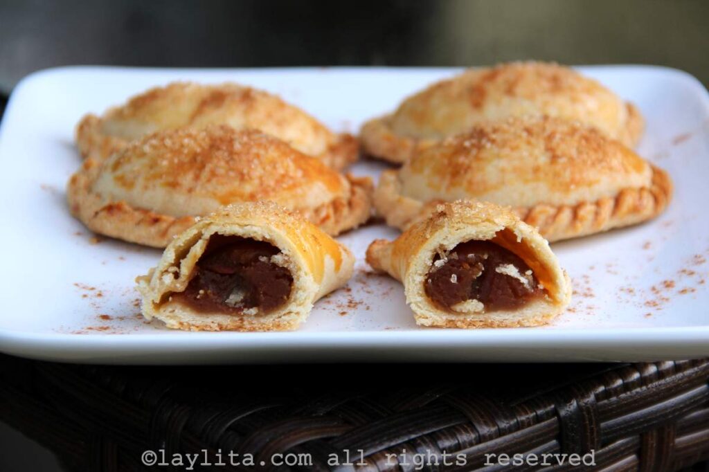 Un plato blanco con empanadas dulces de calabaza con una cortada por la mitad para mostrar el relleno
