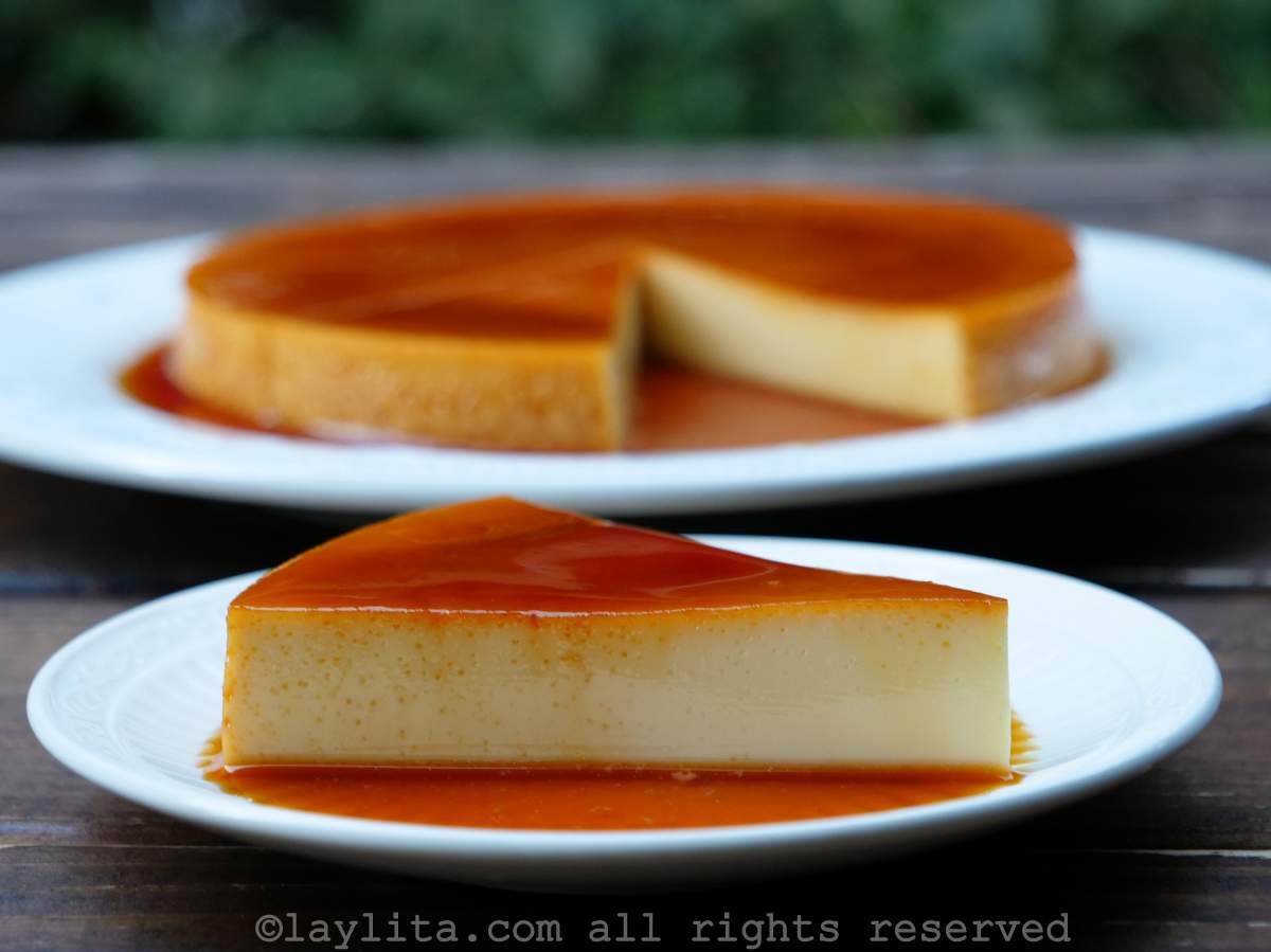 En una mesa se ve un plato blanco con un pedazo de quesillo o flan, en el fondo se ve otro plato blanco con más flan