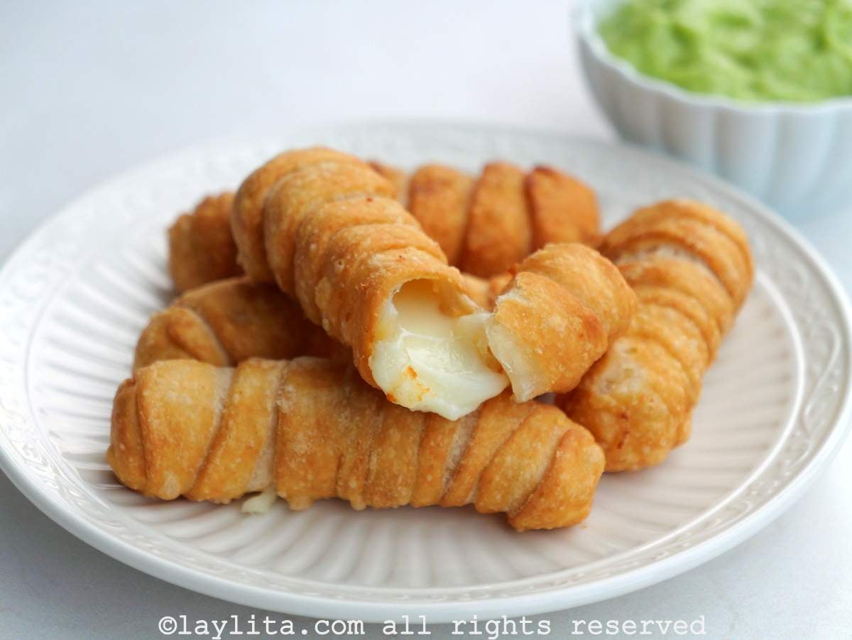 Un plato blanco con varios tequeños venezolanos con salsa guasacaca en el fondo