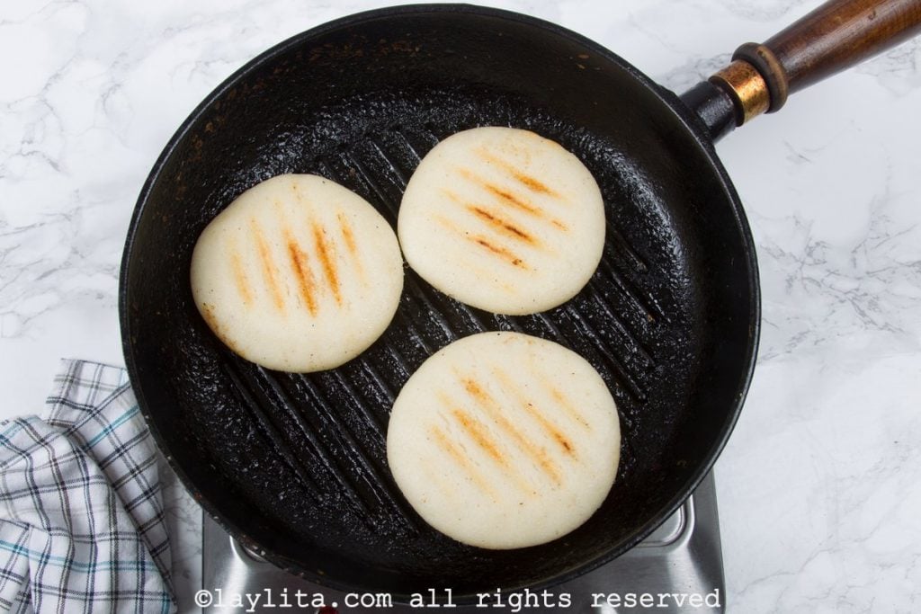 Tres arepas cocinandose en una sartén