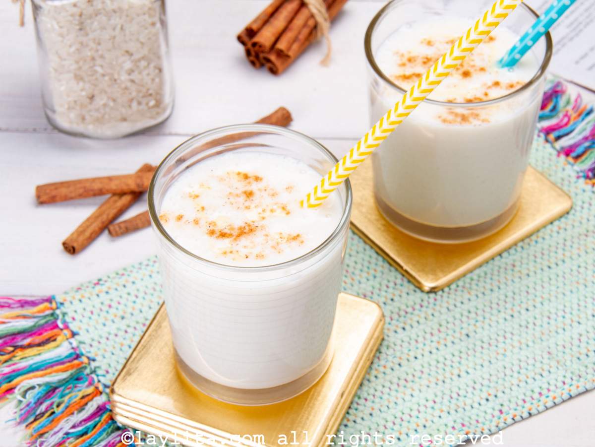 Dos vasos de chicha venezolana decorados con canela con un envase de arroz en el fondo