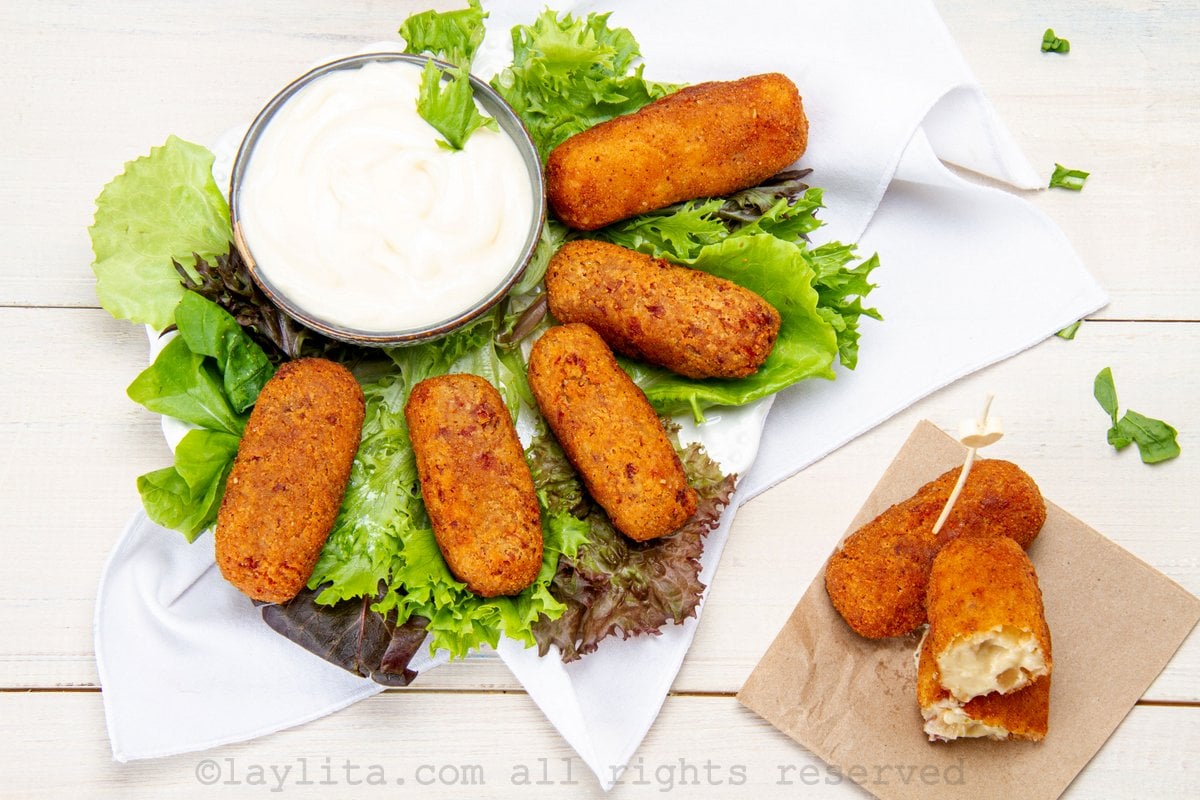 Croquetas de jamón en un plato con hojas de lechuga y dos croquetas al lado encima de una servilleta
