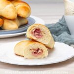 Un cachito de jamón cortado por la mitad mostrando el relleno, con más cachitos en el fondo