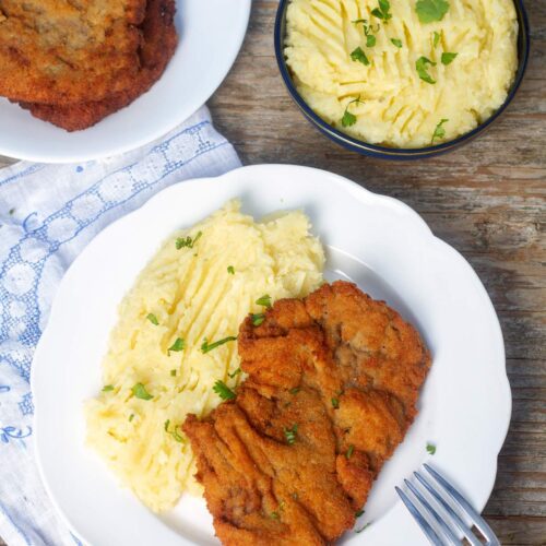 Una milanesa de carne de res o bistec de carne apanada en un plato blanco, con puré de papas al lado