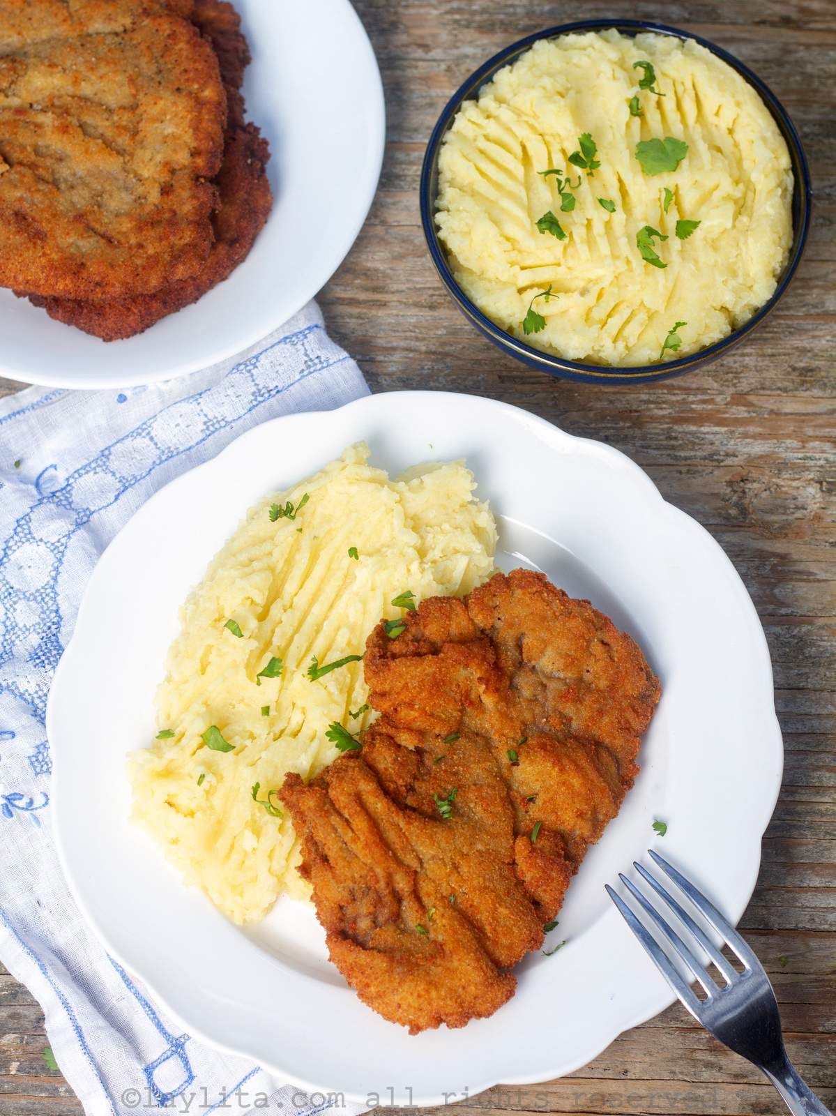 Una milanesa de carne de res o bistec de carne apanada en un plato blanco, con puré de papas al lado