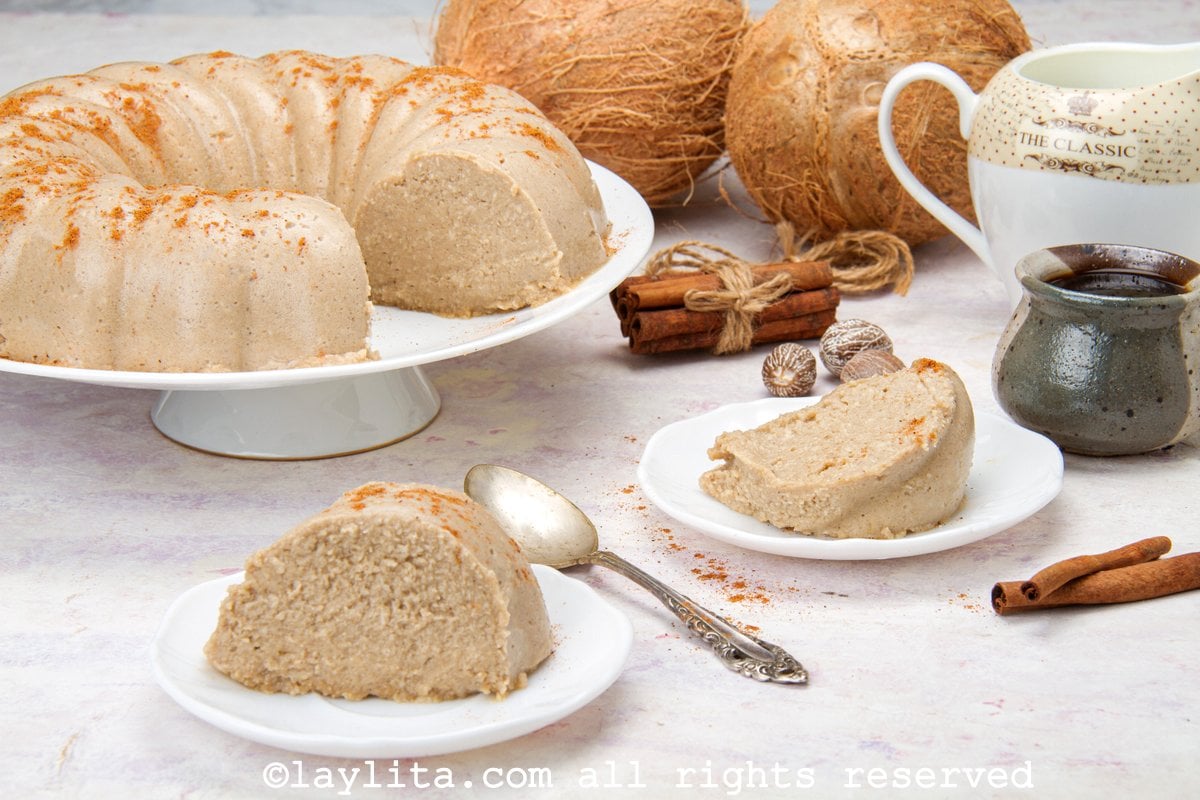 Rebanadas de majarete de coco en platos blancos con el resto en un servidor de pasteles al fondo