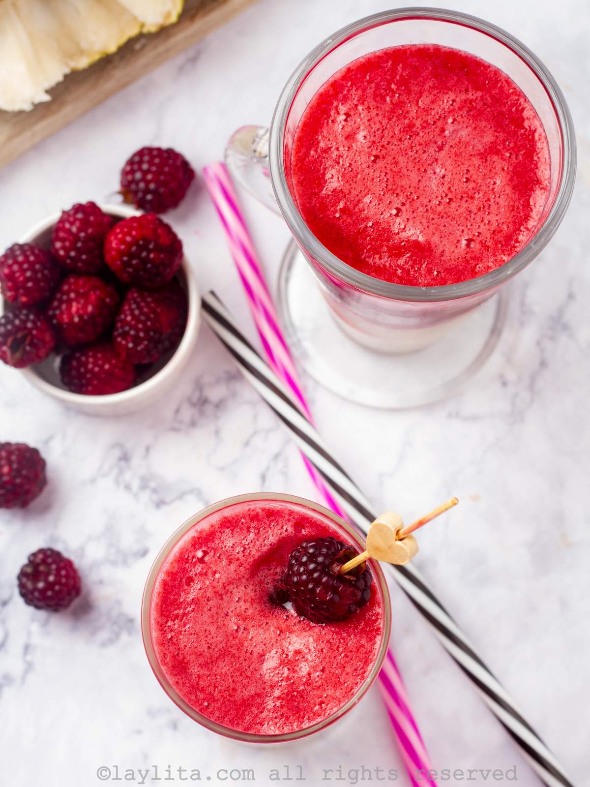 Dos vasos llenos de batido de mora y guanabana, decorados con moras y sorbetes
