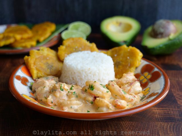 Un plato con camarones encocados, arroz, patacones y aguacate