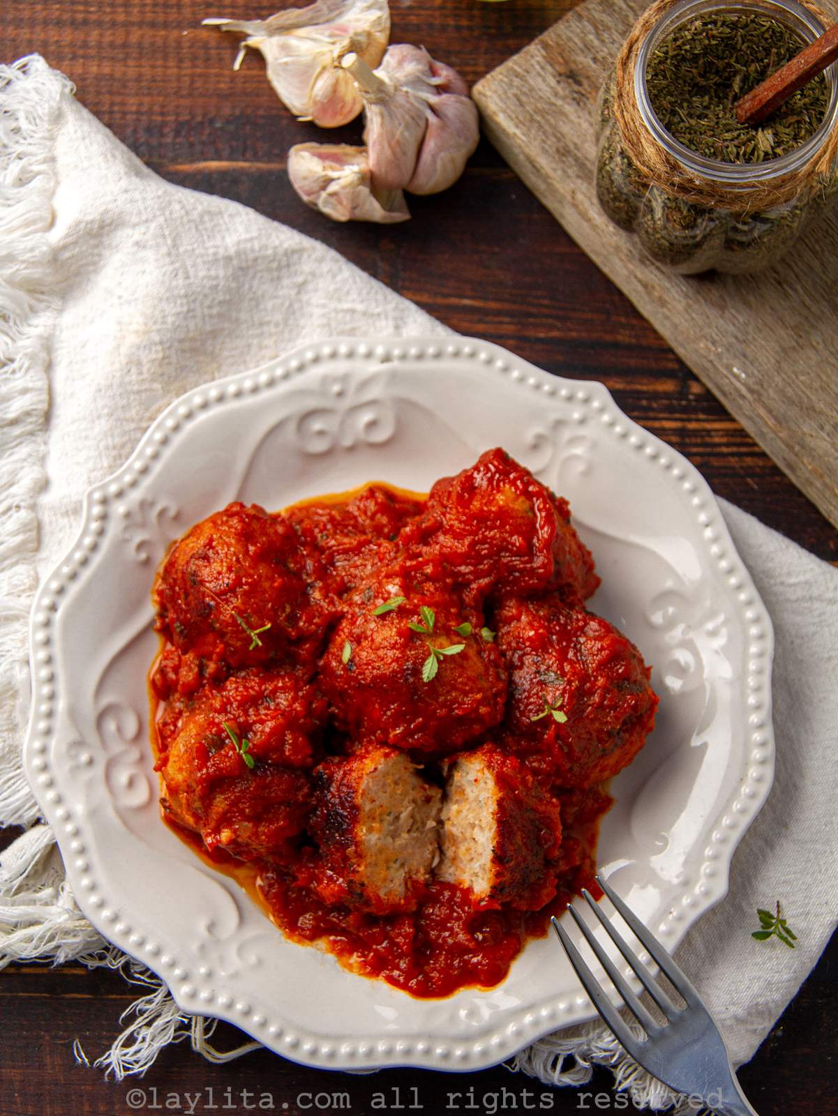 Un plato blanco en una mesa con albóndigas de pollo en salsa de tomate, con un tenedor