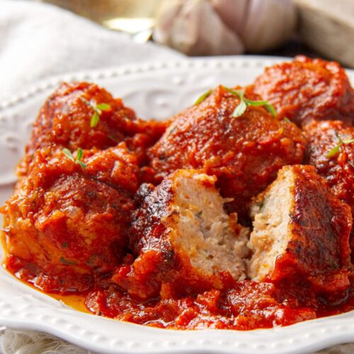 Un plato blanco con albóndigas de pollo en salsa de tomate con una albóndiga cortada por la mitad