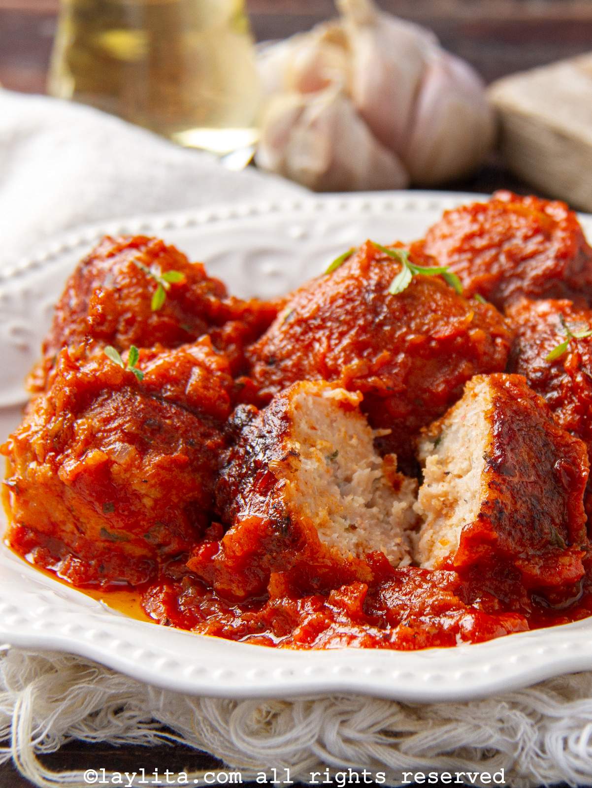 Un plato blanco con albóndigas de pollo en salsa de tomate con una albóndiga cortada por la mitad