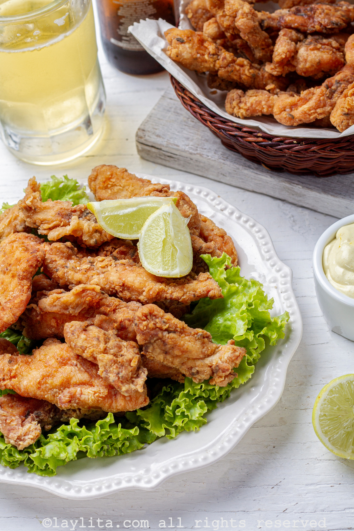Chicharrón de pollo en un plato con rodajas de limón y un vaso de cerveza