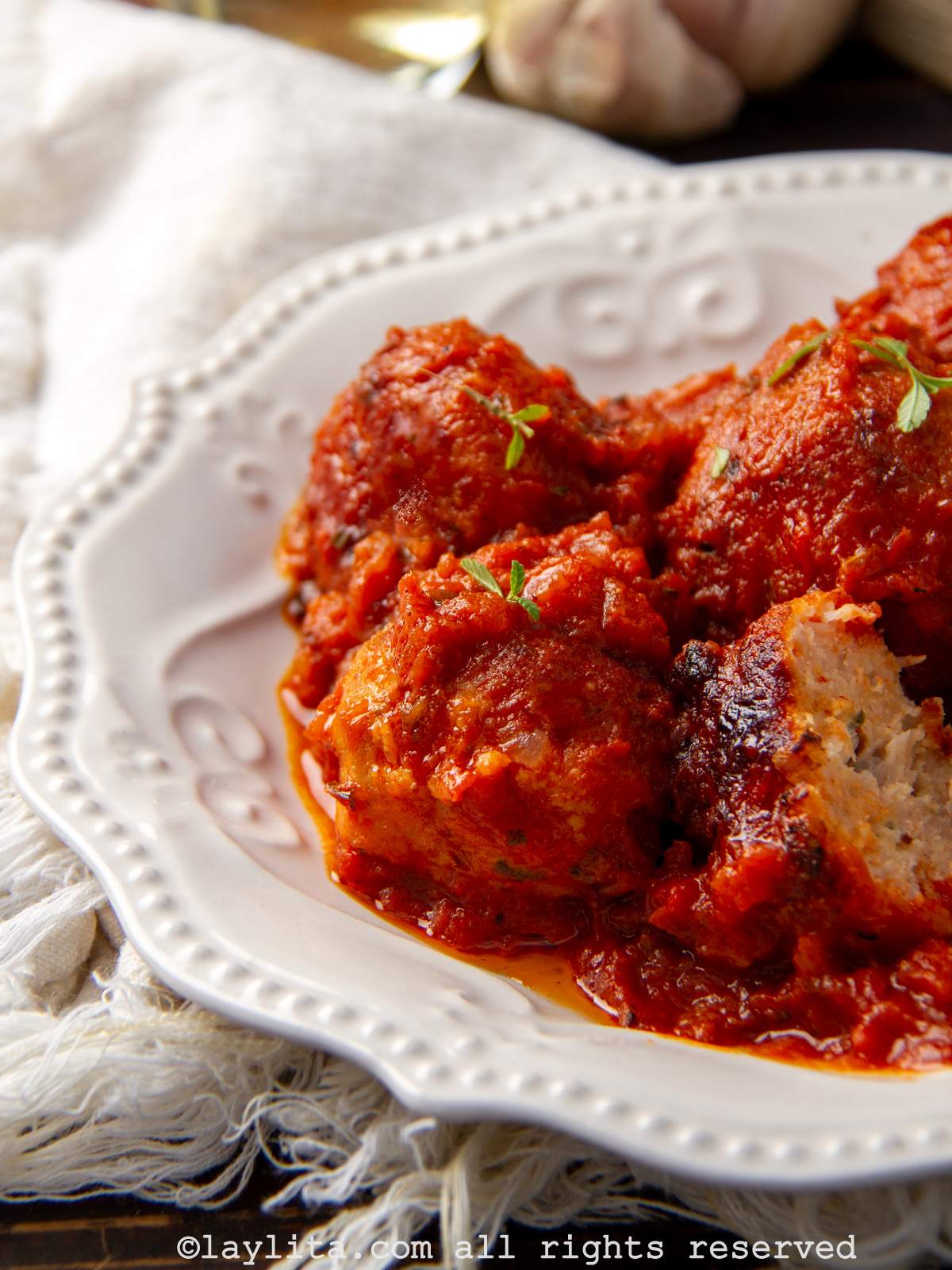 Un plato blanco con albóndigas de pollo en salsa de tomate con una albóndiga cortada por la mitad