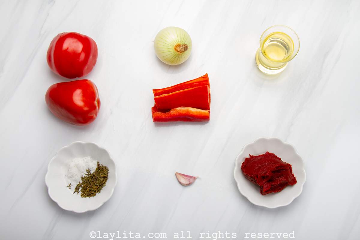 Ingredientes de la salsa para las albóndigas en una mesa: Tomates, cebolla, pimiento rojo dulce, ajo, aceite, pasta de tomate, orégano, sal