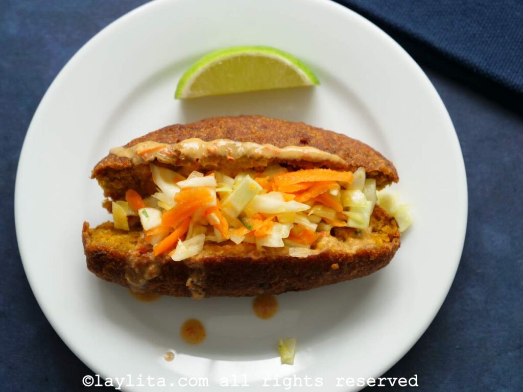 Un corviche de pescado cortado por la mitad y lleno de salsa de maní y ensalada de col con zanahoria
