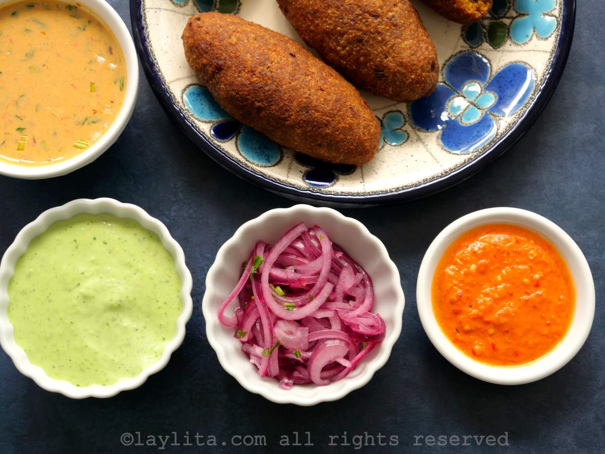 Corviches en un plato con salsas y aderezos: salsa de mani, mayonesa verde, cebollas encurtidas, y aji