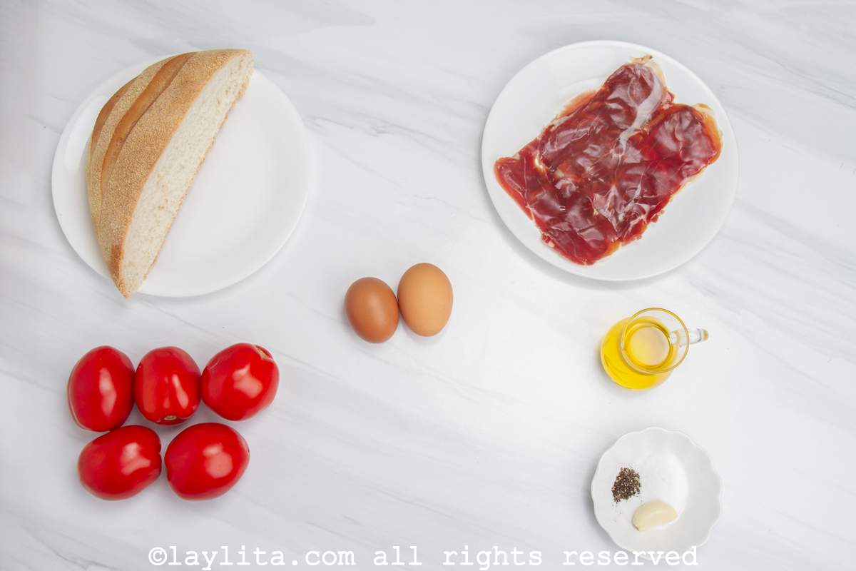 En una mesa blanca se ven los ingredientes del salmorejo cordobés: Tomates, pan, aceite de oliva, ajo, sal, pimienta, huevos duros y jamón serrano