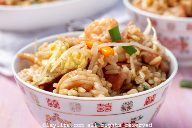 Un bol con arroz frito chino con camarones en una mesa rosada