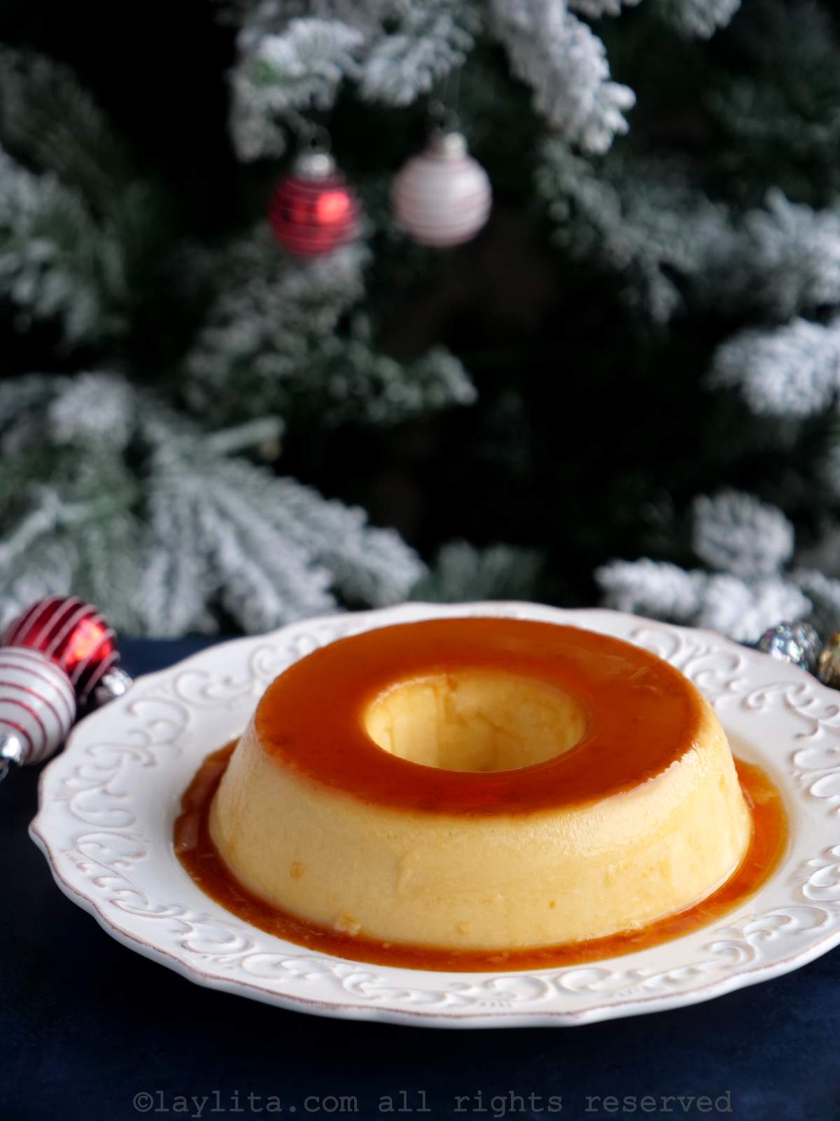 Flan de rompope desmoldado en un plato blanco con un arbol de Navidad en el fondo