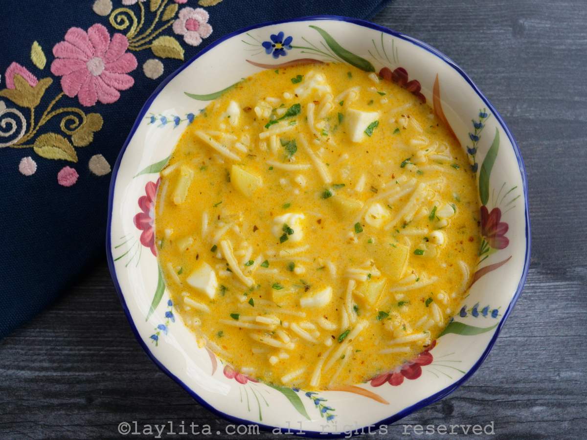 Sopa de fideo con queso en un plato sopero blanco decorado con flores, con una servilleta bordada en el fondo