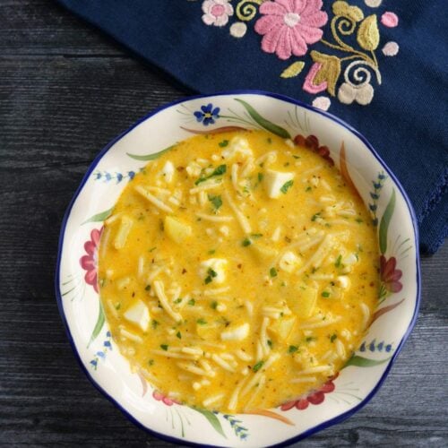 Sopa de queso en un plato sopero blanco decorado con flores, con una servilleta bordada en el fondo