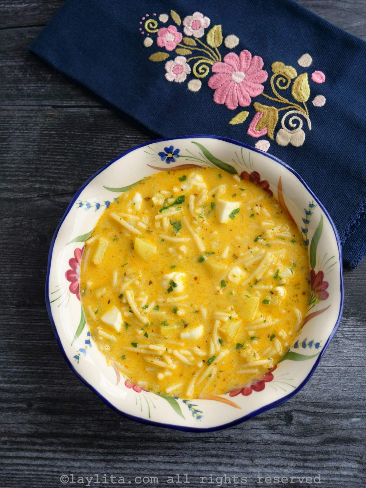 Sopa de queso en un plato sopero blanco decorado con flores, con una servilleta bordada en el fondo