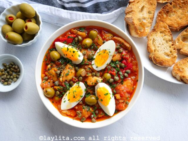 Un plato blanco con bacalao a la vizcaína decorado con huevos duros y perejil