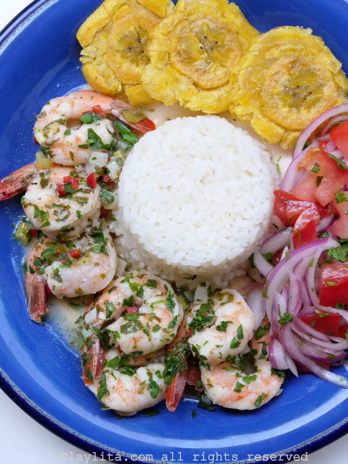 Camarones al ajillo en un plato azul con patacones, arroz y ensalada