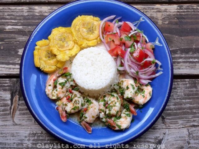 Un plato azul con camarones al ajillo, arroz, patacones y ensalada
