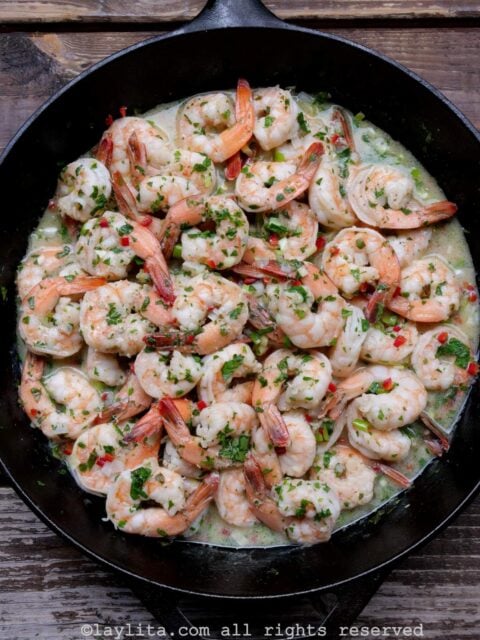Camarones en salsa de ajo y vino blanco en una sartén con un fondo de mesa de madera