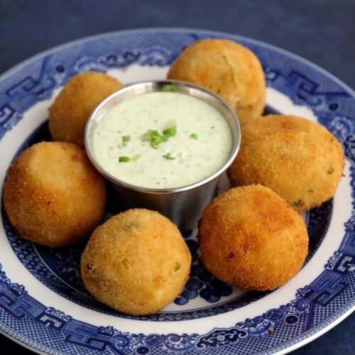 Croquetas redondas de papa y atún en un plato azul con salsa alioli verde de cilantro