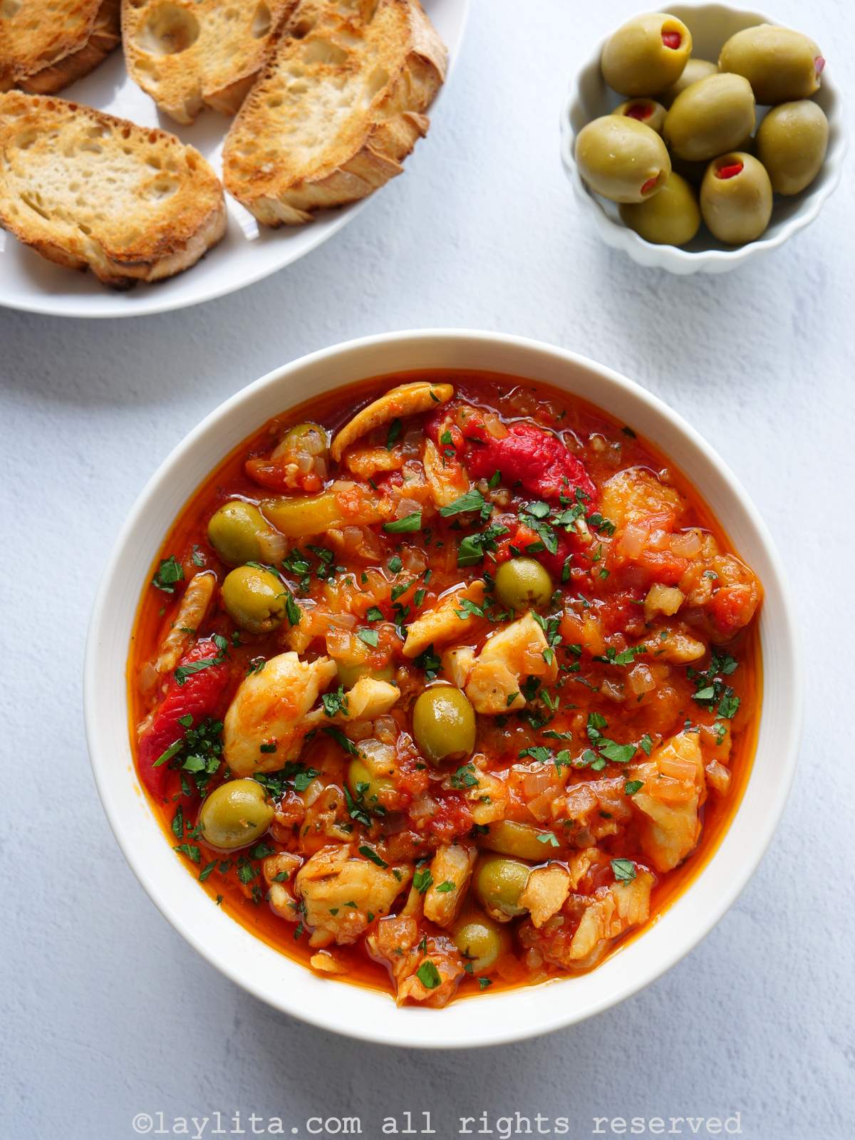 Pescado desalado en salsa de tomate, pimientos, cebolla con aceitunas en un plato blanco