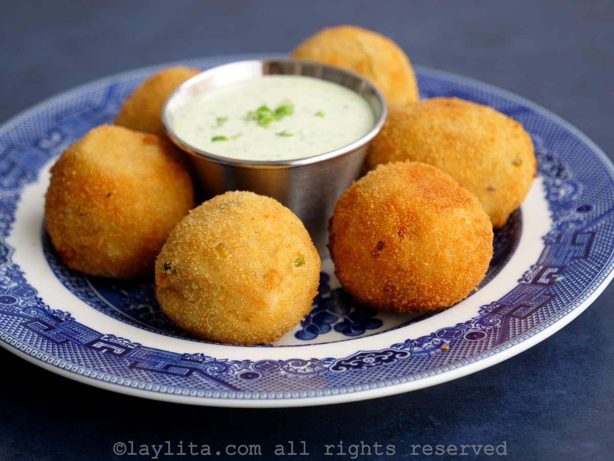 Croquetas redondas de papa y atún en un plato azul con salsa alioli verde de cilantro