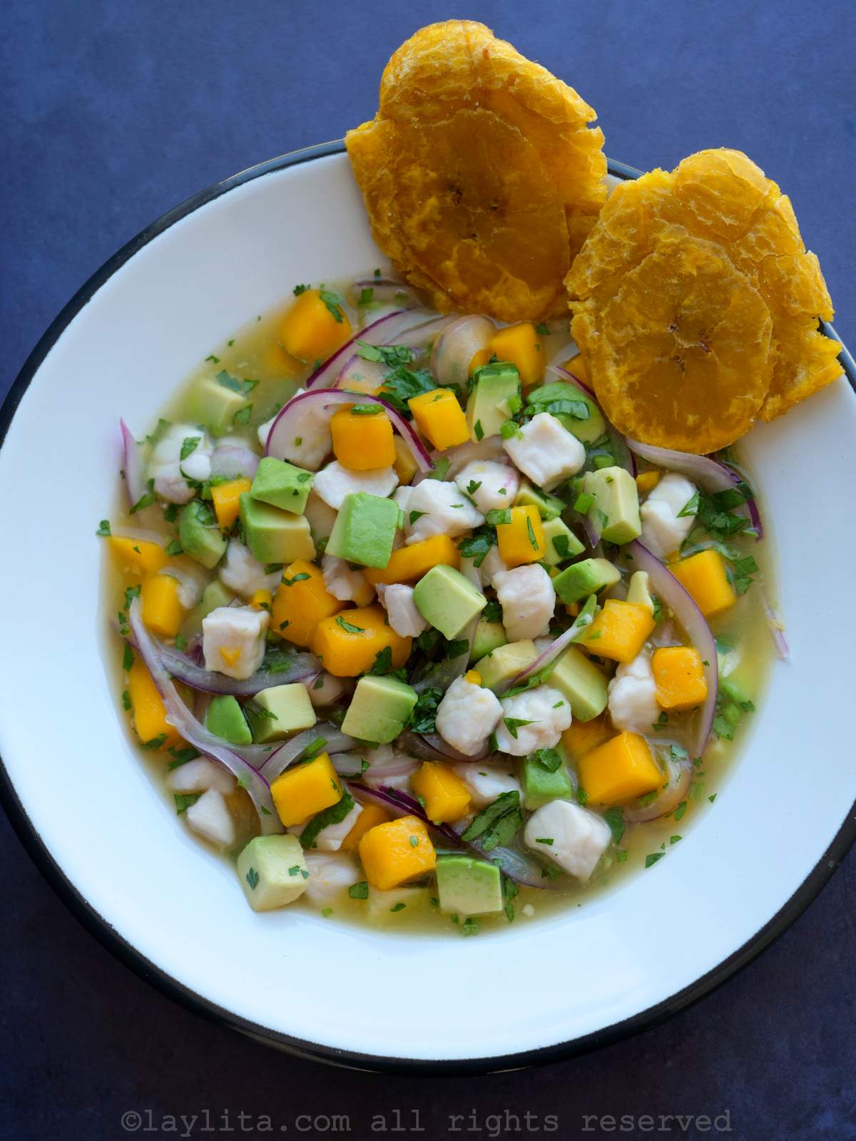 Un plato de ceviche de pescado con mango, con dos patacones al lado