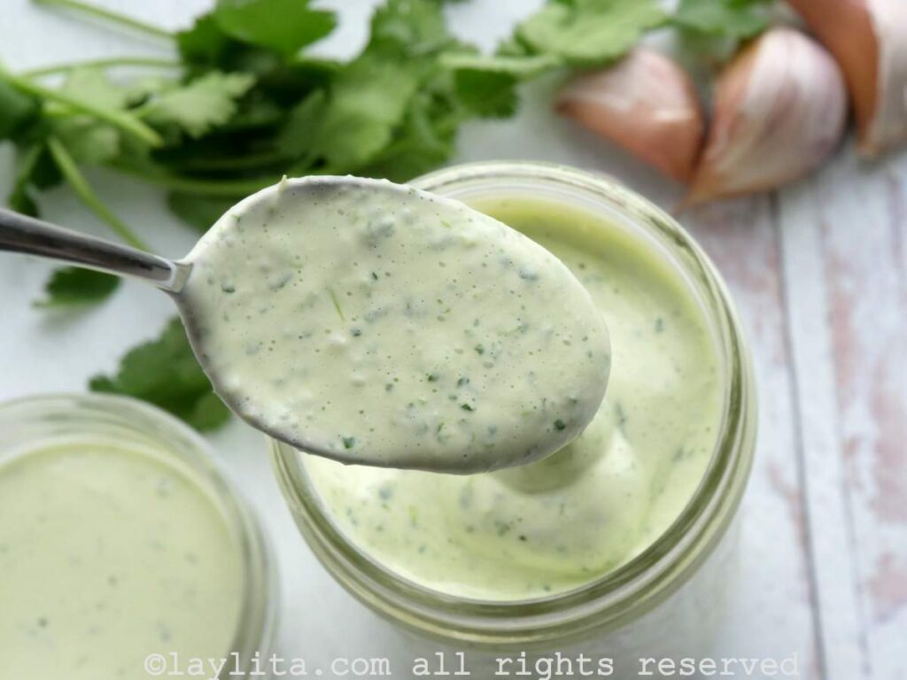 Una cucharada llenas de salsa de alioli verde con el recipiente en el fondo
